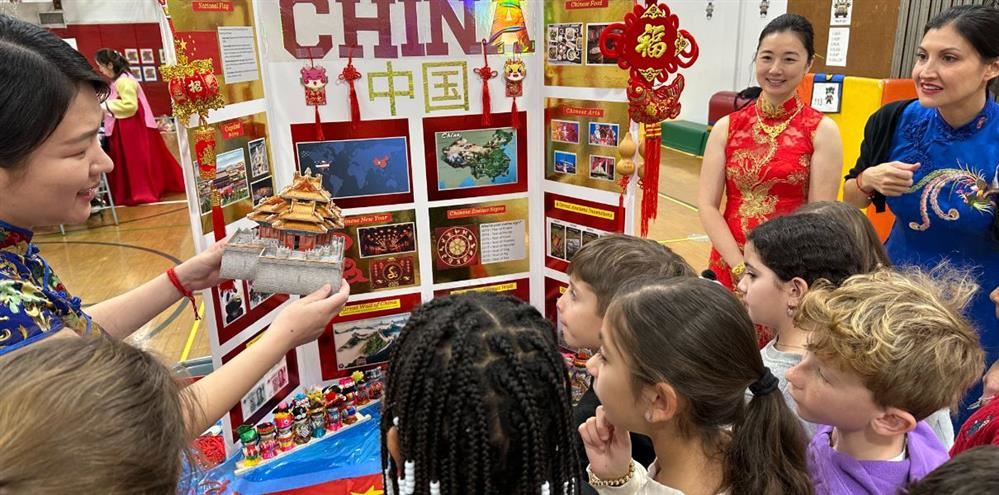  A mom showing off a model of a home in China with students looking on.