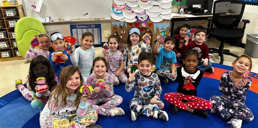  Kindergarteners wearing their pajamas and holding up gingerbread people.
